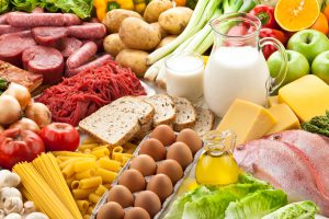 A large group of food. The assortment includes fruits, vegetables, meat, fish and dairy products. The food is mostly sorted by type. The dairy products are in the center, while the rest of the food is circled around the dairy products. Studio photo taken with DSRL Canon EOS 5D Mk II