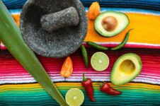 Chili, lime och avokado bredvid en mortel på färgstark duk