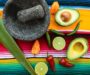 Chili, lime och avokado bredvid en mortel på färgstark duk
